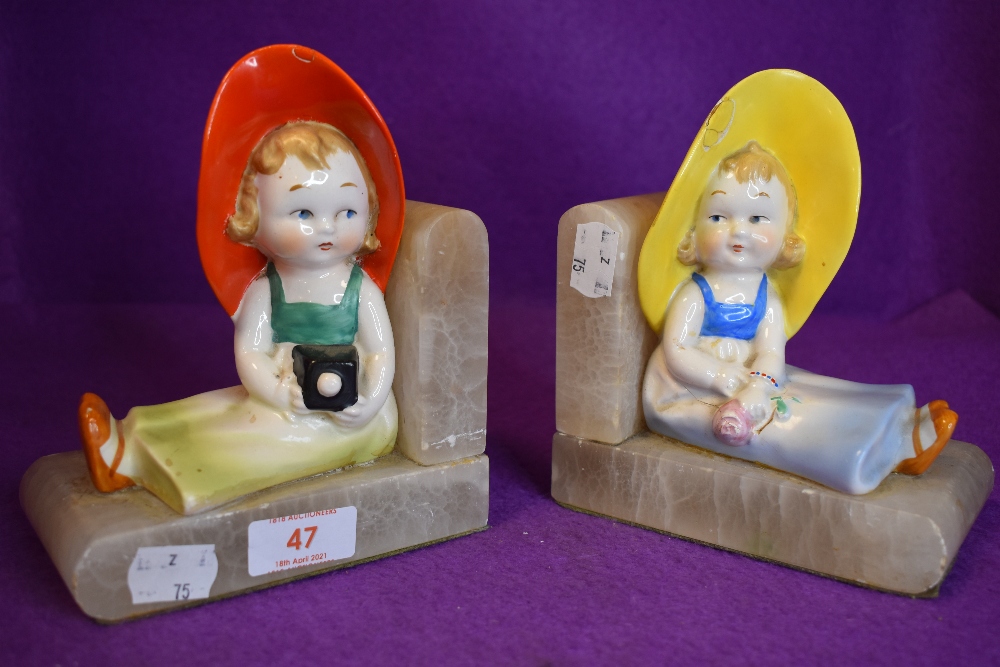 A pair of art deco book ends depicting young girls in sunhats, one holding camera the other a rose.