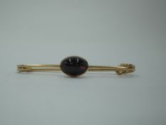 A yellow metal bar brooch in the form of a safety pin having a garnet cabouchon, no marks tests as