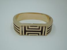 A rose gold plated bangle by Tory Burch made to hold a FIT BIT style fitness tracker, having Greek