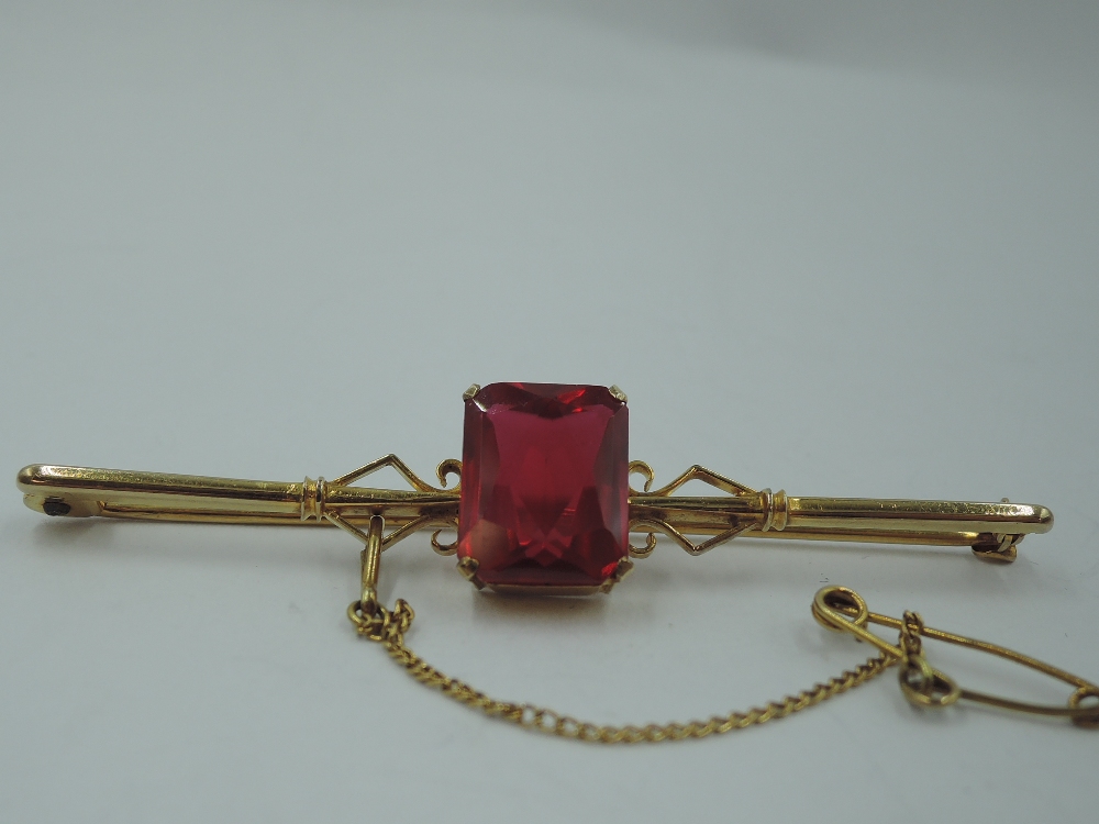 A yellow metal bar brooch stamped 9ct having a central ruby style rectangular stone, approx 4.6g