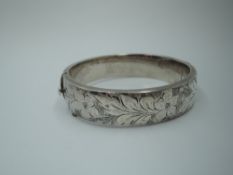 A silver hinged bangle having engraved floral decoration, safety chain missing
