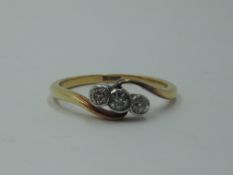 A three stone diamond ring in collared mounts to crossover shoulders on a yellow metal loop