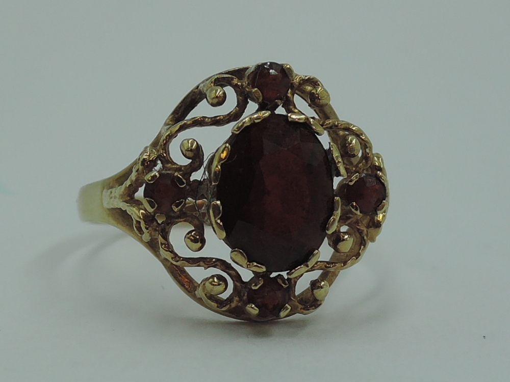 A lady's dress ring having a central garnet in an open decorative border on a 9ct gold loop, size