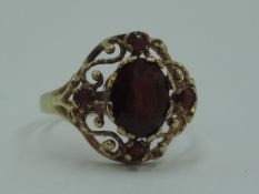 A lady's dress ring having a central garnet in an open decorative border on a 9ct gold loop, size