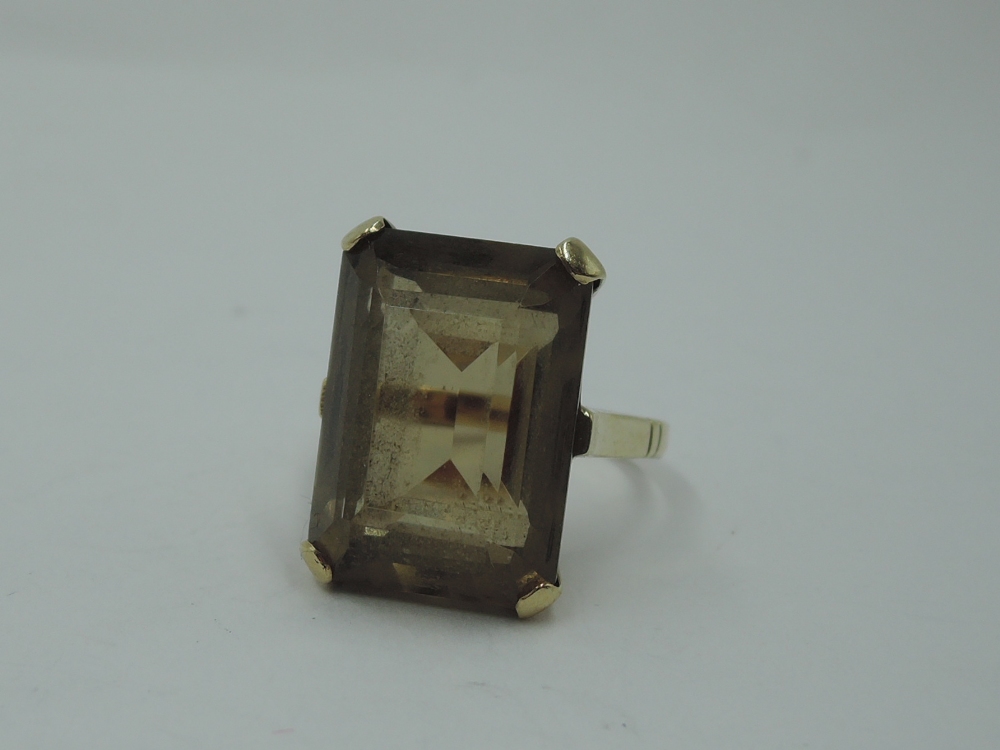 An oversized smoky quartz ring in a raised four claw basket mount on a yellow metal loop stamped