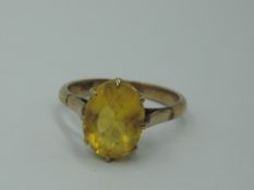 A yellow metal dress ring stamped 9ct having an oval yellow paste stone in a raised claw set