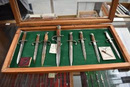 A wood and glass small display case containing a collection of 8 Miniature Bayonets with Quillions