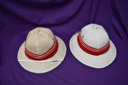 Two Pith Helmets, white with red and white bands, both size 60cm, both with chin straps