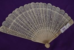 An intricate antique fan having carved ribs and mother of pearl rivet.