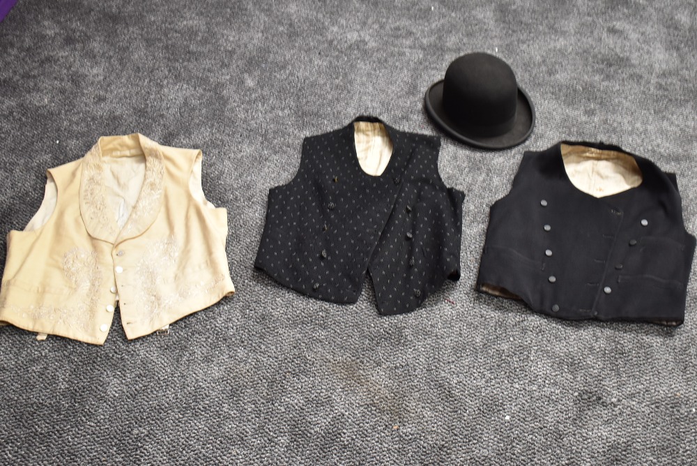 A collection of gents antique clothing including waistcoats and top hat.