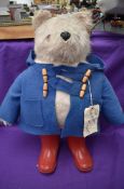 A Gabrielle Designs plush covered Padding Bear soft toy, wearing blue jacket and red wellingtons,