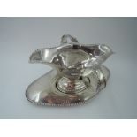 An Edwardian silver double spout sauce boat and saucer having gadrooned decoration to rims and