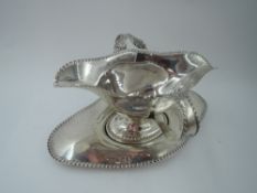 An Edwardian silver double spout sauce boat and saucer having gadrooned decoration to rims and