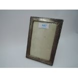 A small silver photograph frame of rectangular form having moulded decoration and wooden back with