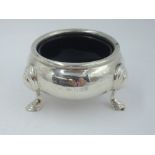 A silver salt cellar of plain cauldron form having trefoil hoof feet and blue glass liner, London