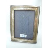 A silver photograph frame of plain rectangular form having a wooden back with easel stand and blue