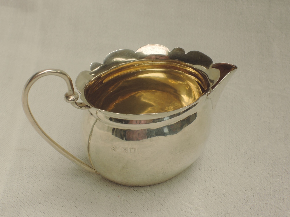 A small Edwardian silver cream jug of oval form having frilled rim, looped wire handle and gilt - Image 2 of 2