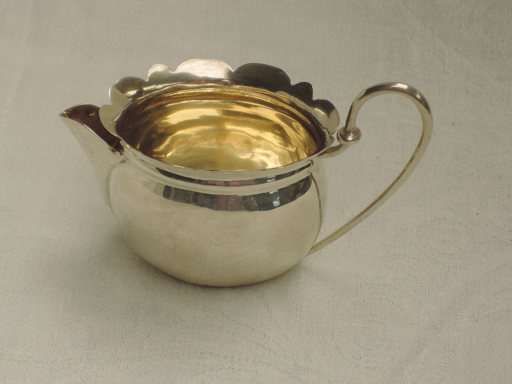 A small Edwardian silver cream jug of oval form having frilled rim, looped wire handle and gilt