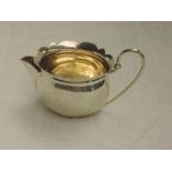 A small Edwardian silver cream jug of oval form having frilled rim, looped wire handle and gilt