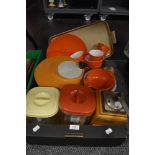 A collection of retro tupperware including orange Melaware plates and cups.
