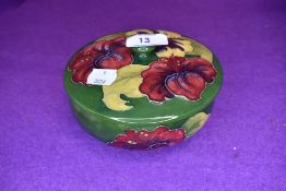 A vintage Moorcroft lidded bowl having green and blue ground and red and yellow hibiscus pattern.