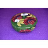 A vintage Moorcroft lidded bowl having green and blue ground and red and yellow hibiscus pattern.
