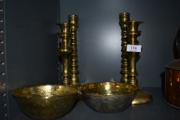 Four brass candlesticks and two intricately decorated ethnic or ethnic styled bowls, having embossed