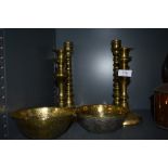 Four brass candlesticks and two intricately decorated ethnic or ethnic styled bowls, having embossed