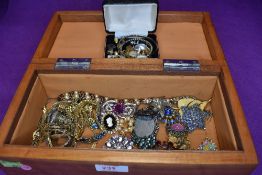 A treen jewellery box containing a small selection of costyume jewellery including brooches, wrist