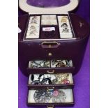 A maroon travel jewellery case of barrel form containing a selection of costume rings, bracelets and