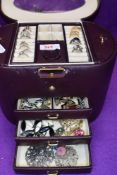 A maroon travel jewellery case of barrel form containing a selection of costume rings, bracelets and