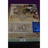 A vintage chocolate box containing a selection of costume brooches and necklaces including crystal