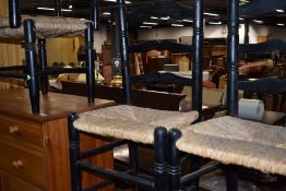 A pair of ebonised and rush seated ladder back chairs, and similar footstools