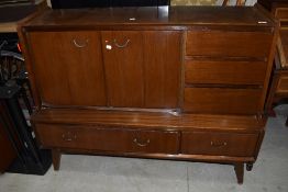 A mid Century sapele side cabinet having bifold doors, triple drawer section and drawers to base, on