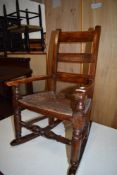 A childs oak framed rocking chair with woven fibre seat and ladder style back