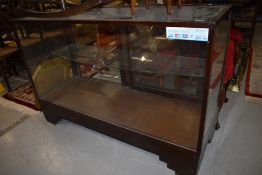 A vintage stained frame and glazed shop counter having sliding doors, width approx 137cm, some