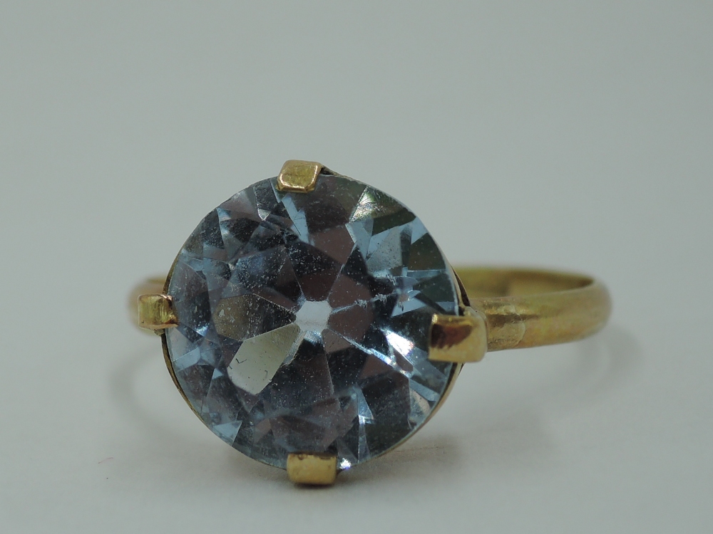 A blue topaz style solitaire ring having four claw set mount on a yellow metal loop stamped 9ct,