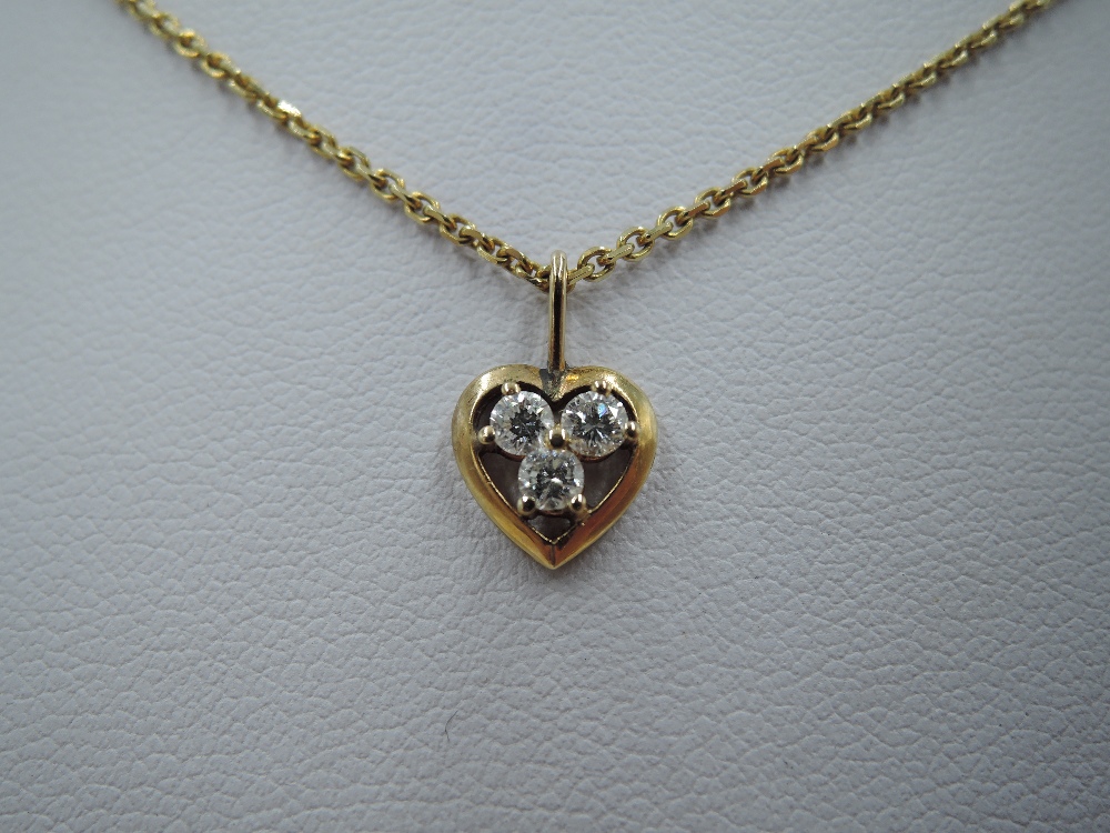A yellow metal heart pendant having a trio of small diamonds in an open mount on a yellow metal