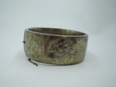 A silver hinged bangle of broad form having engraved scroll and floral decoration, approx 39g