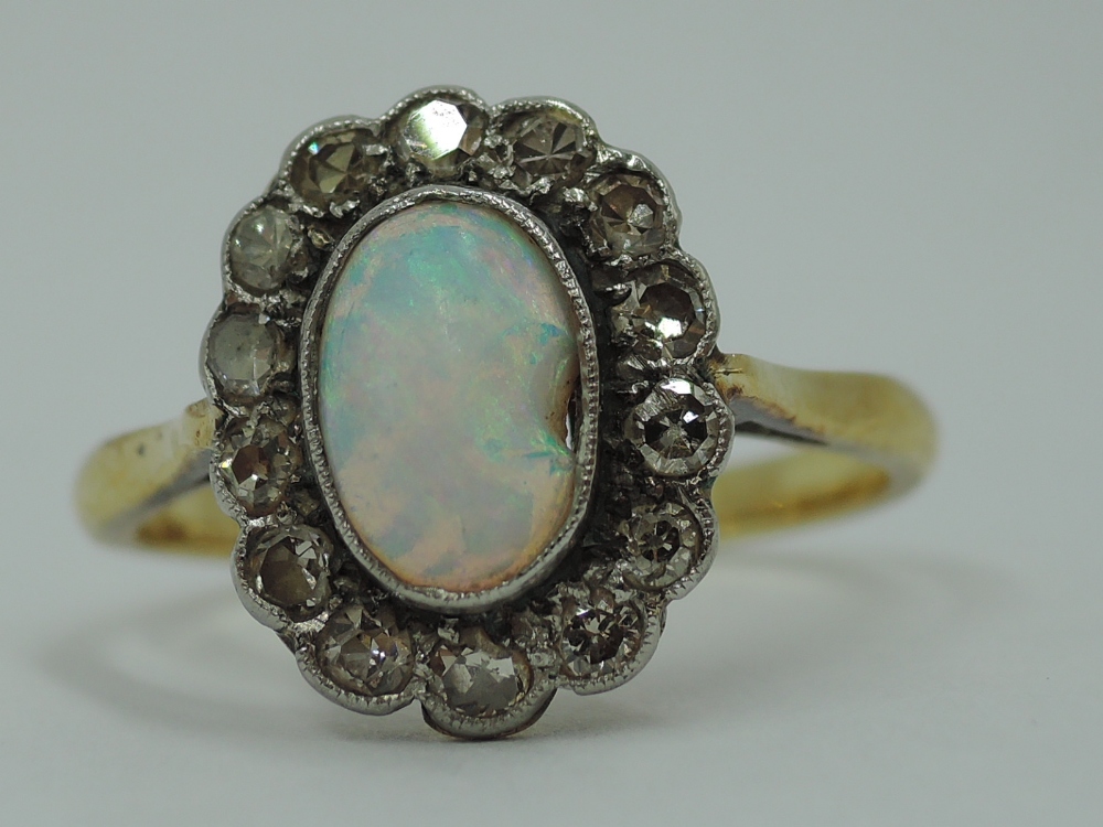 An opal and diamond cluster in a collared basket mount on a yellow metal loop stamped 18ct, size P &