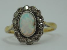 An opal and diamond cluster in a collared basket mount on a yellow metal loop stamped 18ct, size P &