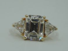 A synthetic clear three stone dress ring having a central emerald cut stone flanked by two