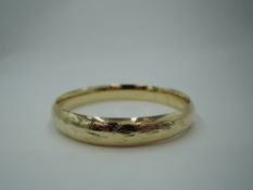 A yellow metal hinged bangle stamped 14K having slide clasp and engraved decoration, approx 13.5g