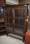 An early 20th Century dark oak display or bookcase having leaded glass doors, on short twist legs,