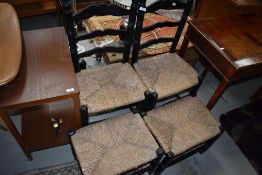 A pair of ebonised and rush seated ladder back chairs, and similar footstools