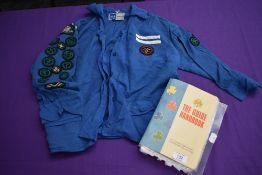 A 1960s girl guides blouse with badges and a copy of the guide book.