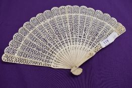 An intricate antique fan having carved ribs and mother of pearl rivet.