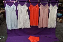 A collection of vintage nylon slips in a variety of colours, one having matching knickers.