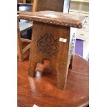 An arts and crafts stool having carved sides with decorative leather worked top