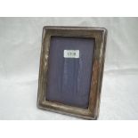 A silver photograph frame of plain rectangular form having a wooden back with easel stand and blue